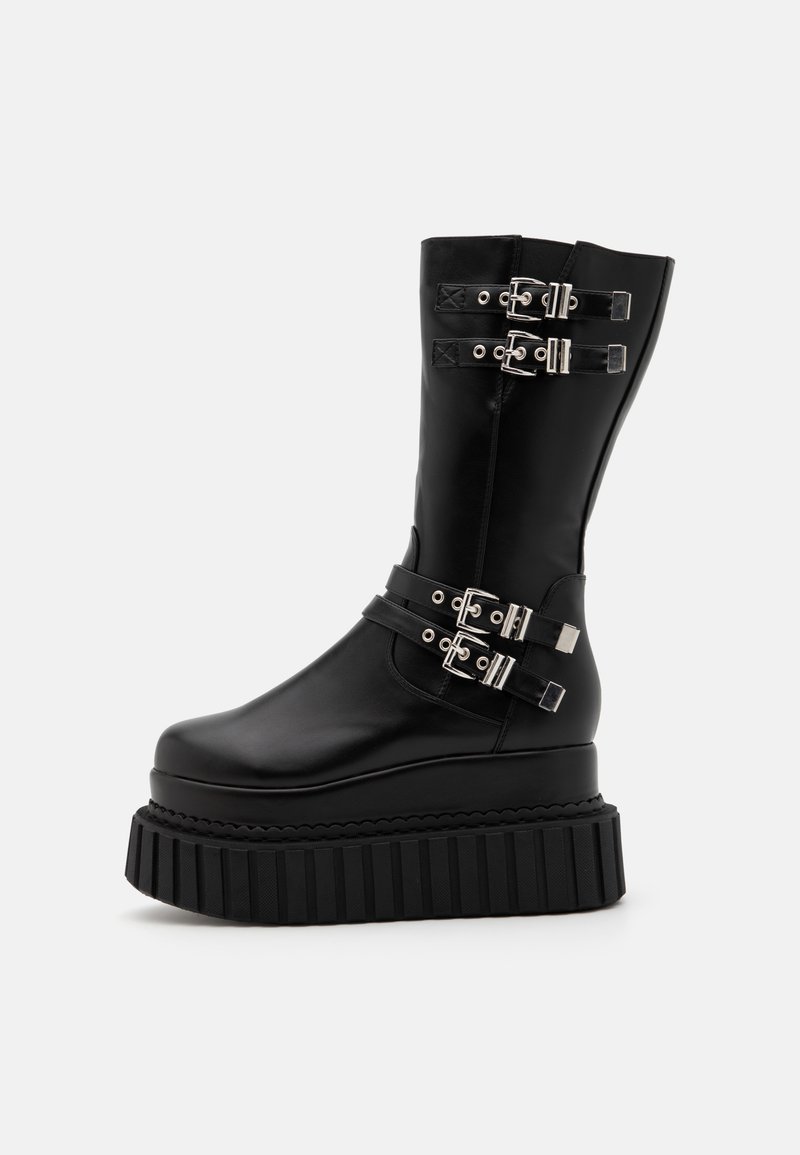 Black platform boots made of smooth faux leather, featuring multiple silver buckle accents and a ribbed sole for added grip.