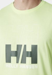 Světle zelené tričko s velkým grafikou ve šedé a bílé barvě, s nápisy "HH" a "Helly Hansen". Vyrobeno z měkké bavlny.