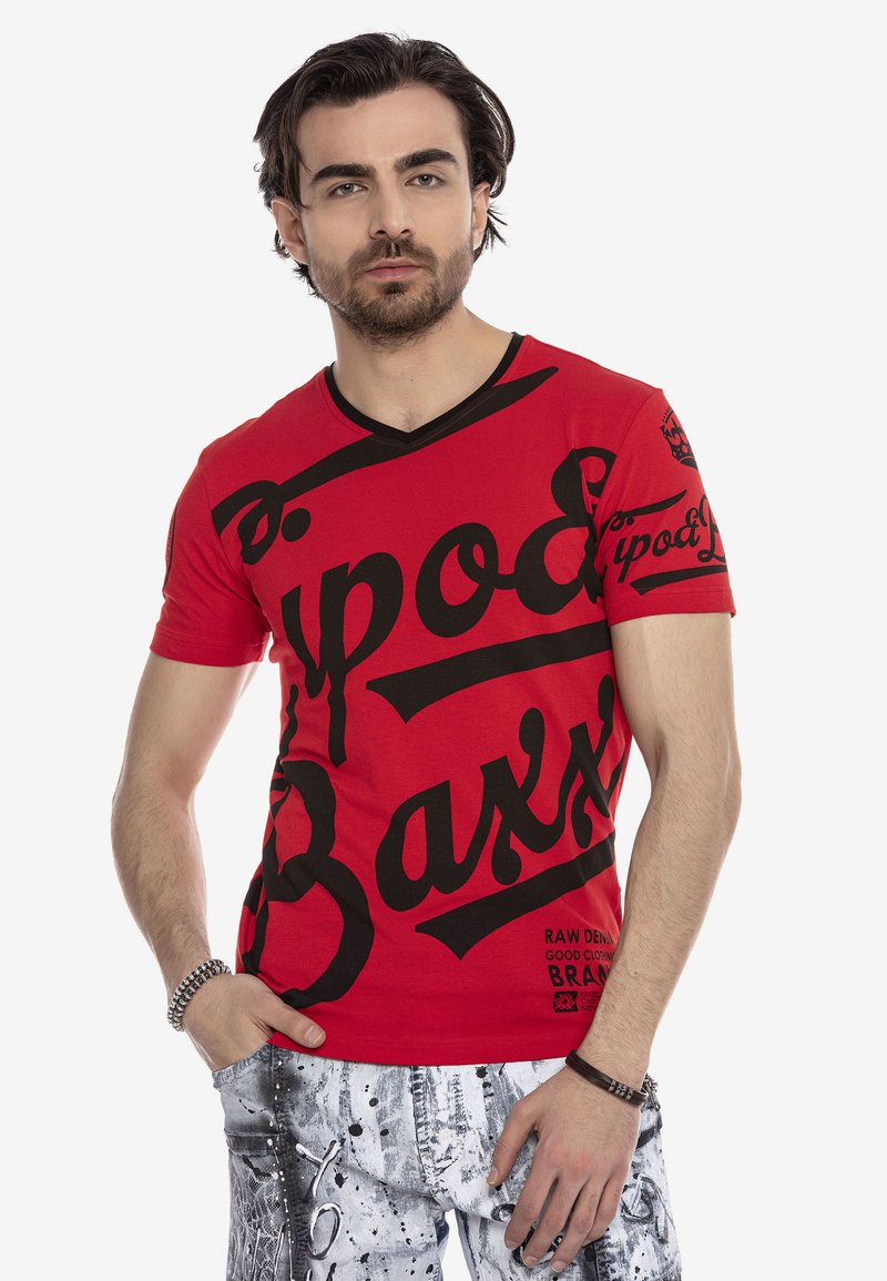 Rotes T-Shirt mit kurzen Ärmeln, kombiniert mit schwarzem grafischem Text und Mustern. Es hat ein V-Ausschnitt-Design und eine schlanke Passform. Das Material wirkt glatt.