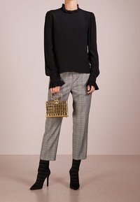 Blusa nera a maniche lunghe con colletto arricciato, pantaloni grigi a quadri, borsa dorata in pelle lucidato a croco e stivaletti neri arricciati.