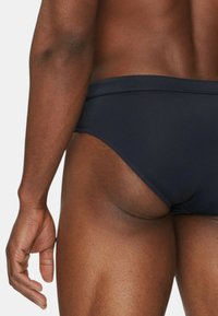 Bañador de natación navy con una tela suave y elástica, que presenta costuras mínimas y un ajuste ceñido, mostrado de lado con parte de un brazo visible.