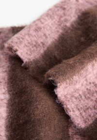 Textil din lână cu o textură moale, cu dungi alternante de culoare roz deschis și maron închis. Marginile par ușor destrămate.