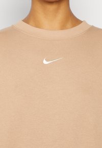 Klasická b�éžová mikina s kulatým výstřihem a malým bílým vyšitým logem Nike na hrudi, vyrobená z měkké bavlny.