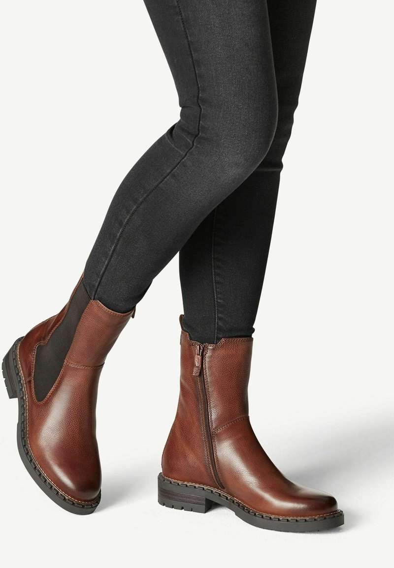 Braune Leder Stiefeletten mit seitlichen elastischen Einsätzen, Reißverschluss hinten und strukturiertem Finish. Robuste schwarze Gummisohle für guten Halt.