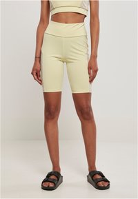 Pantaloni sportivi gialli realizzati in materiale elasticizzato, lunghi fino al ginocchio, con una vita alta e una texture liscia. Indossati con sandali neri.