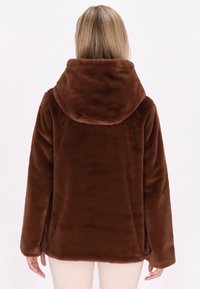 Bruine fleece jack met een grote capuchon, zachte textuur en lange mouwen. Beschikt over zijzakken en een relaxte pasvorm.