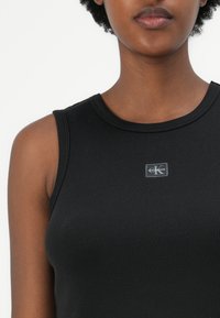 Fekete bordázott ujjatlan póló kerek nyakkivágással. Elöl egy kis téglalap alakú Calvin Klein logó található. Simás textúrájú, testhezálló fazon.