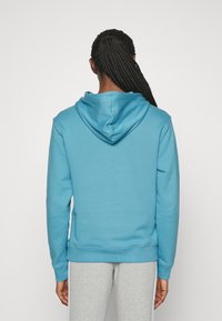 Hoodie i ljusblått, tillverkad av mjukt tyg. Har en känguruficka och ribbade muddar. Slät textur, enkel design.