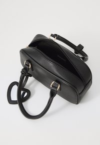 Sac à main en simili cuir noir de forme rectangulaire, avec des accessoires en métal doré, une fermeture éclair sur le dessus et un accent miroir en forme de cœur sur la sangle.