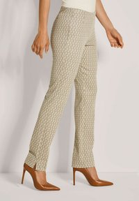 Vrouw in beige, patroon slim-fit broek met kleine zijsplitten aan de onderkant en bruine, spitse hooggehakte schoenen.