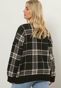 Sweater ruudust musta ja pruuniga, millel on lõtv istuvus, ribatud äär ja tekstuurne kangas. Pikad varrukad ja langenud õlavarred.