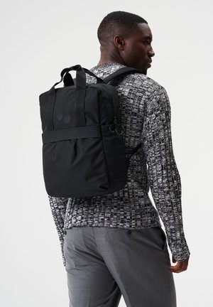 Schwarzer Rucksack aus strukturiertem Material, ausgestattet mit zwei oberen Griffen, verstellbaren Riemen und einem schlichten Design mit kreisförmigen Akzenten.