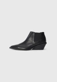 Botas de tobillo de cuero negro con punta afilada, paneles laterales elásticos y un tacón corto y en ángulo. Textura suave con un detalle mínimo.
