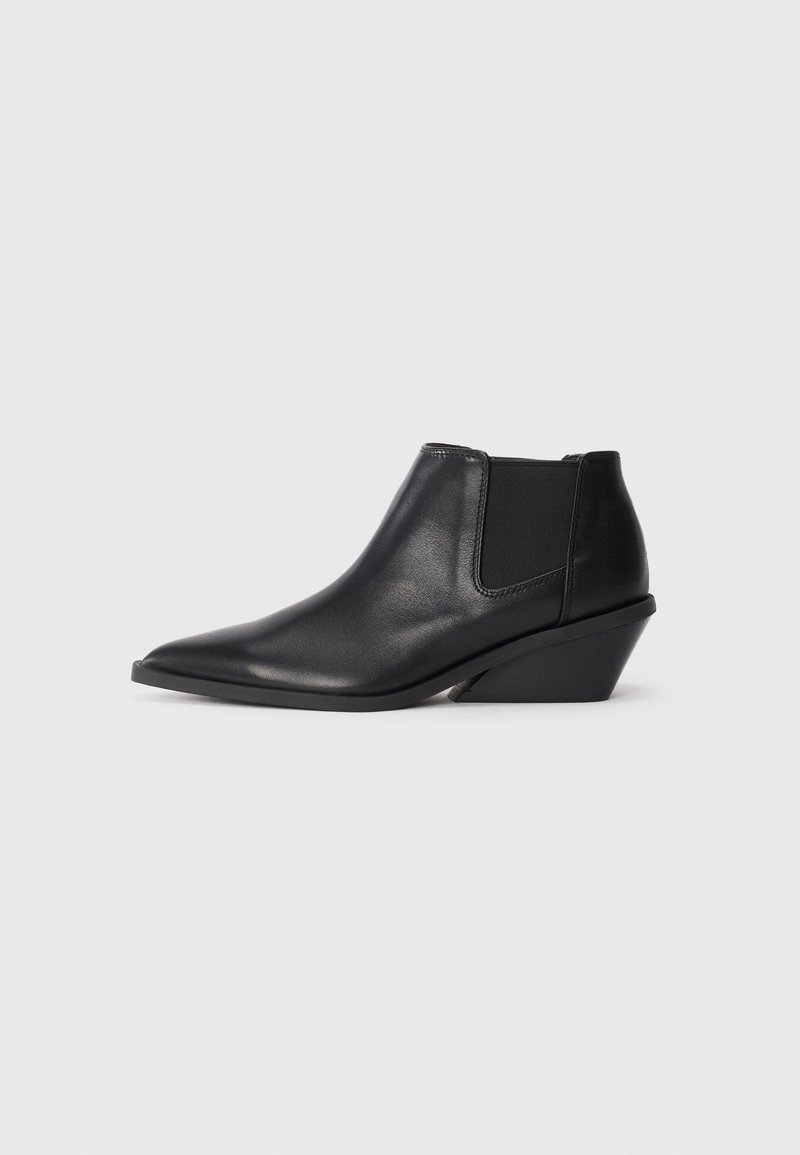 Botas de tobillo de cuero negro con punta afilada, paneles laterales elásticos y un tacón corto y en ángulo. Textura suave con un detalle mínimo.