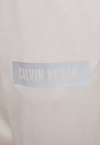 Light beige sweatshirt featuring a woven texture and a blue rectangular logo that reads "CALVIN KLEIN" in a white font.