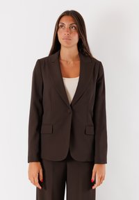 Blazer marrone sartoriale con revers a battaglia, due tasche anteriori e chiusura a un bottone. Tessuto morbido e vestibilità strutturata.