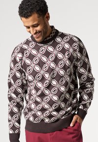 Stickad tröja med en mörkbrun bas och ett mönster av vita och burgunderfärgade blad. Inkluderar en ribbad krage och manschetter, samt en figurnära nederkant.