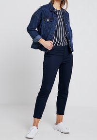 Jeansjacka i mörkblått, med knappstängning framtill och bröstfickor, kombinerad med mörkblå tajta byxor och vita sneakers, vilket ger en avslappnad stil.