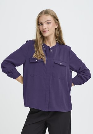 Purple long-sleeve shirt with a rounded collar, two chest pockets, button detail, and a relaxed fit. Smooth fabric with a subtle sheen.