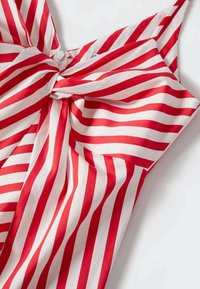 Un tissu rayé rouge et blanc présentant un détail en nœud au niveau du col, avec une texture lisse et un design sans manches.