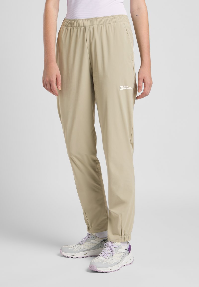Crème-kleurige, lichte wandelbroek met een elastische tailleband, zijzakken en een logo-detail nabij de rechterheup.