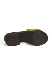 Houten klompen met een bruine basis, een ronde neus en een beige band met gouden studs. Geprofileerde buitenzool voor grip.