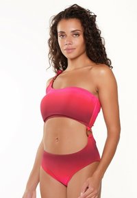 Een one-shoulder bikini met een ombre van roze naar rood, gemaakt van een gladde stof. Het heeft een hoge taille ontwerp met gouden hardware accenten aan de zijkant voor extra detail.