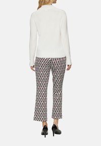 Weißer, enganliegender Pullover mit Rundhalsausschnitt, kombiniert mit gemusterten Hosen in Rot, Weiß und Schwarz sowie schwarzen High Heels.