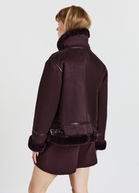 Giubbotto in shearling bordeaux con colletto alto, caratterizzato da dettagli in pelle e una fibbia in vita, texture morbida e design corto.