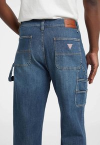 Donkerblauwe denim cargobroek met meerdere zakken, contrasterende stiksels en een leren merkpatch op de tailleband. Geweven stof.