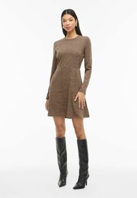 Robe marron à manches longues avec un motif côtelé texturé, une jupe évasée et un col rond. Associée à des bottes noires à talons aiguilles montantes jusqu'aux genoux.