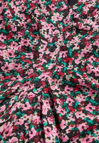 Czarna tkanina z kwiecistym wzorem w odcieniach różu, czerwieni i zieleni, z czarnymi guzikami i detalami plisu. Miękka tekstura.
