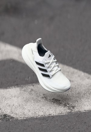 Biele bežecké topánky s textúrovaným zvrškom, tromi čiernymi pruhmi a polstrovanou podrážkou, umiestnené nad šedým povrchom s bielymi znakmi.