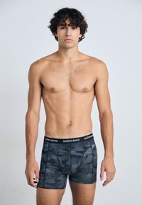 Schwarze Boxershorts mit Camouflage-Muster und einem schwarzen Bund, der das Logo "BJÖRN BORG" trägt, aus einem weichen, dehnbaren Stoff gefertigt.