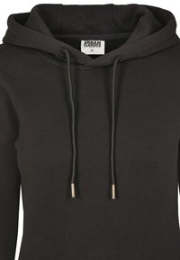 Haut à capuche noir avec un cordon de serrage, doté de pointes en métal sur les lacets. Fabriqué en tissu doux et lisse ; étiqueté "Urban Classics," taille XS.