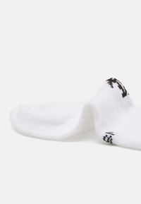 Calcetín de algodón blanco con textura acanalada y logotipo negro en el tobillo. Diseñado para ajustarse cómodamente, enfatizando la comodidad y la transpirabilidad.