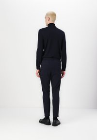 Dark blue turtleneck and tailored trousers, both fitted. Smooth knit texture on the top, trousers have a sleek finish. Black shoes complete the look.
