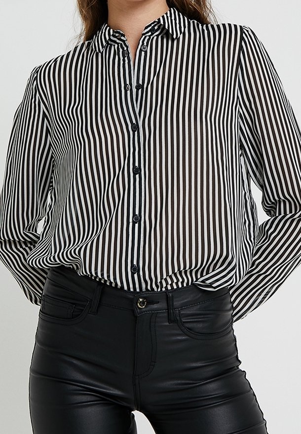 Femme portant une chemise à rayures verticales noires et blanches boutonnée et rentrée dans un pantalon en cuir noir taille haute.
