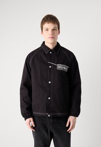 Giacca nera imbottita con chiusura a bottoni, cuciture a contrasto, tasche laterali e logo ricamato "HUGO" sul petto.