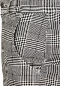Schwarz-weiße karierte Hose aus strukturiertem Stoff. Mit kontrastierenden Mustern, einer Fronttasche und sichtbaren Nähdetails.