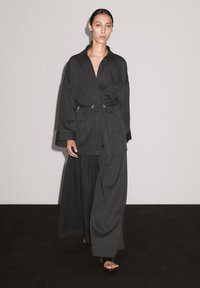Chemise surdimensionnée à rayures noires avec une ceinture, associée à un pantalon à jambes larges. Tissu lisse, manches longues et design minimaliste.