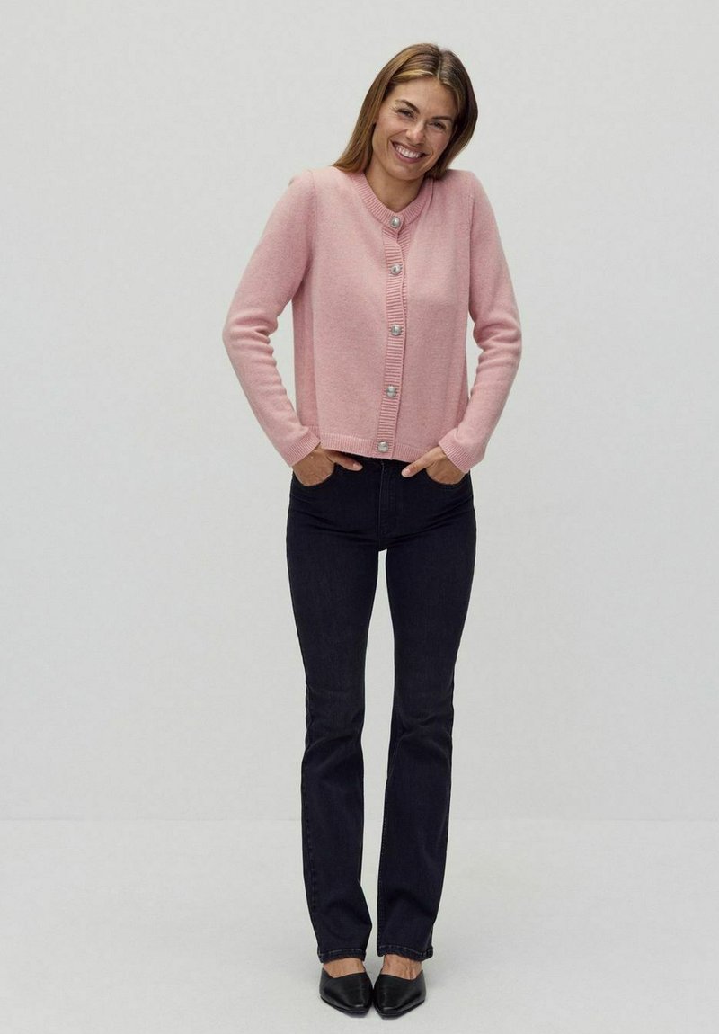 Ljusrosa kofta med rund halsringning, strukturerad ribbad front och sexknappsstängning. Kombinerad med mörka slim fit jeans och svarta skor.