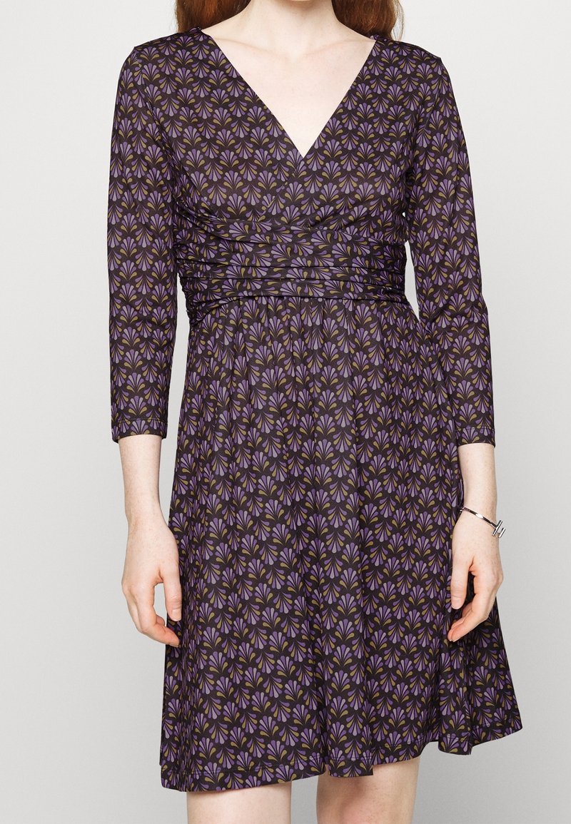 Fioletowa sukienka z długimi rękawami, dekoltem w serek i marszczonym pasem, z wzorem kwiatowym w kolorze zielonym i beżowym. Lekki materiał o miękkiej fakturze.