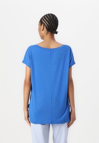 Top blu corto a maniche corte con scollatura rotonda, vestibilità rilassata e una trama sottile. Presenta una cucitura centrale lungo il retro e delle fessure sui lati.