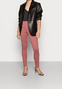 Svart läderblazer, åtsittande grå topp med spetsdetaljer, och rosa stretchbyxor med två guldknappar. Modellen bär svarta klackskor med remmar.