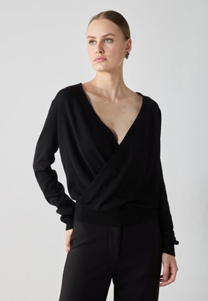 Pull noir enroulé fabriqué dans un matériau doux avec un décolleté en V profond et des manches longues, doté d'une ceinture côtelée et d'une texture lisse.