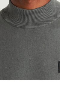 Gray knit sweater with a high ribbed collar. Features a textured surface and a small black logo patch on the lower right side.