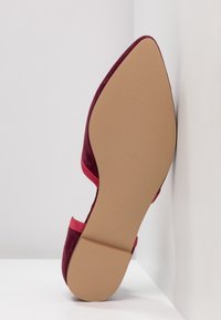 Talons en daim bordeaux avec un bout pointu et des accents roses. La semelle est lisse et plate, présentant une texture semi-mate sans détails supplémentaires.