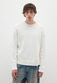 Maglione bianco a maglia con scollatura rotonda, orlo e polsi a costine. Caratterizzato da una vestibilità rilassata e una texture liscia, abbinato a jeans azzurri.