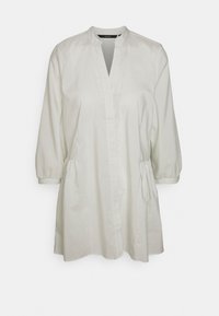 Camisa branca com riscas verticais cinzas claras, mangas longas com bolsa, colarinho alto e bolsos laterais, feita de tecido suave.